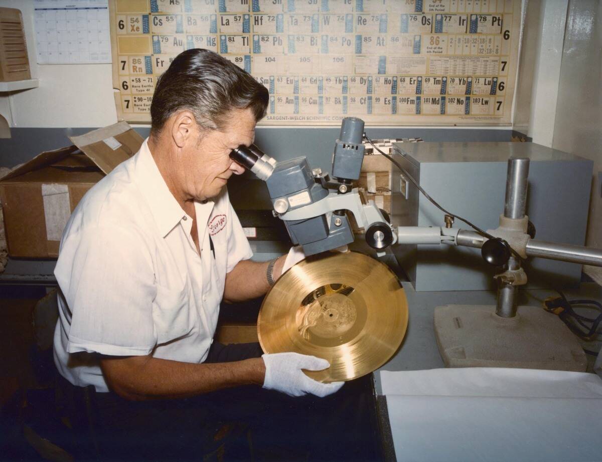 A man examining one of the Voyager Gold Records under a microscope.