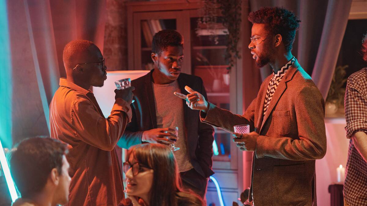 Three friends talking to each other at a get together, the man on the right pointing at the man on the left.