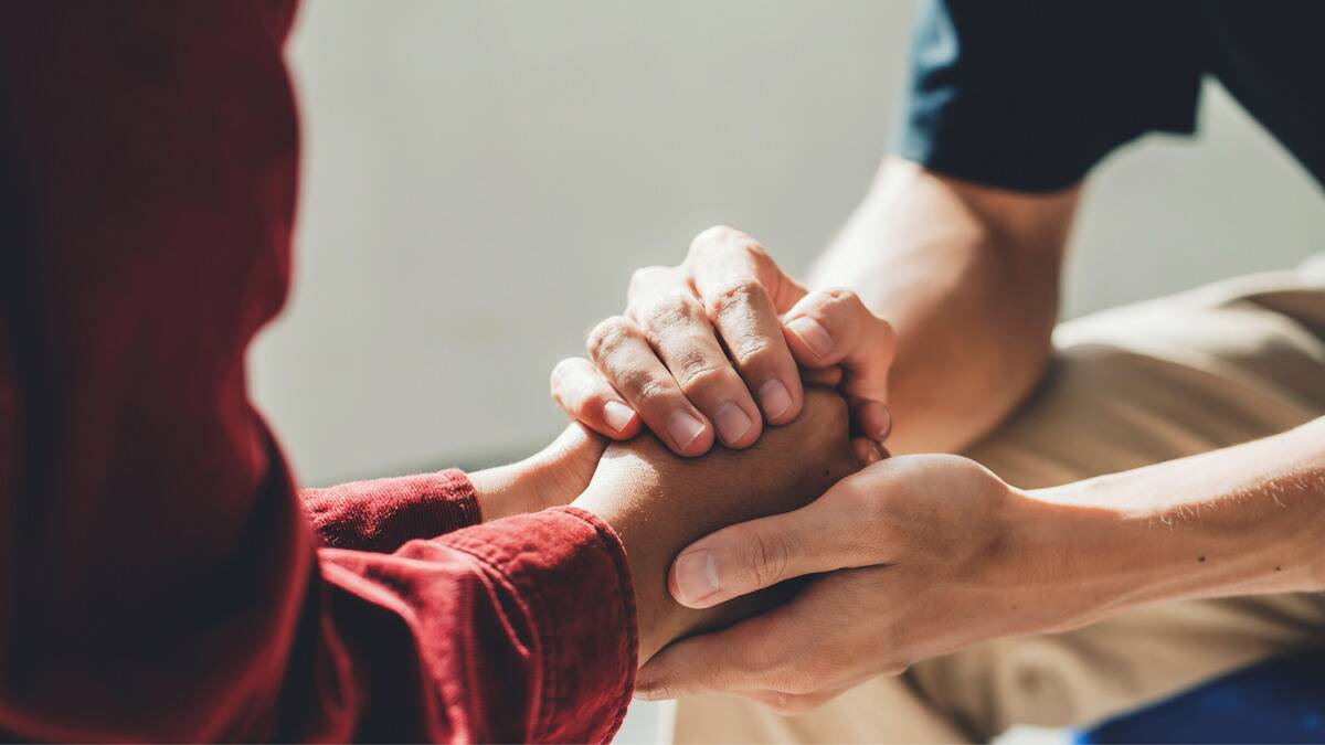 A close shot of a friend holding both of his friends hands between his own in a comforting motion.