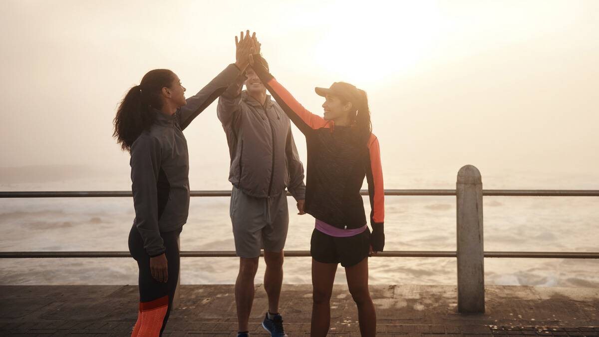 Three runners standing on a boardwalk, their hands up and together in a group cheer.