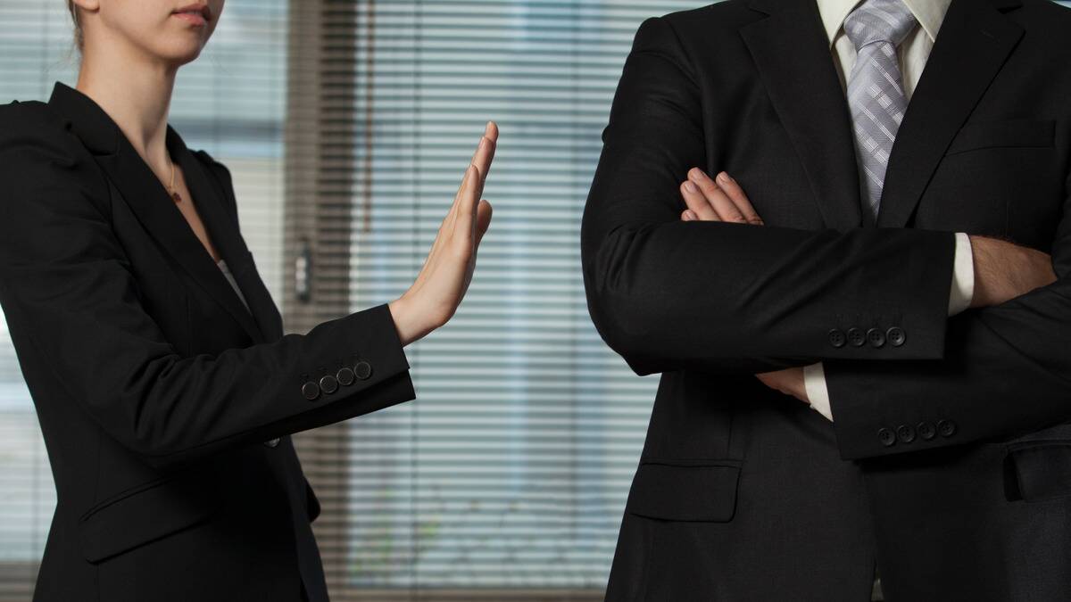 A business woman holding her hand out to stop a businessman who's crossing his arms.