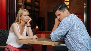 A couple sitting at table for a date, both looking bored, leaning their chin or cheek in their hand.