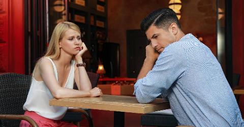 A couple sitting at table for a date, both looking bored, leaning their chin or cheek in their hand.