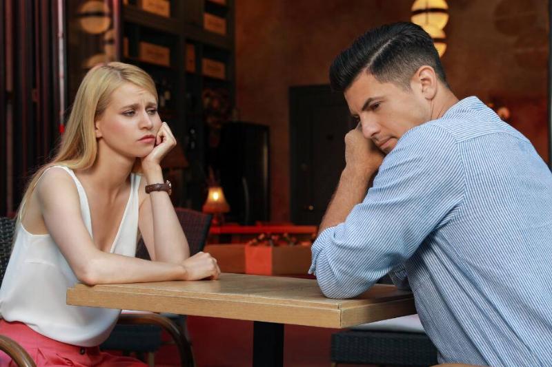 A couple sitting at table for a date, both looking bored, leaning their chin or cheek in their hand.