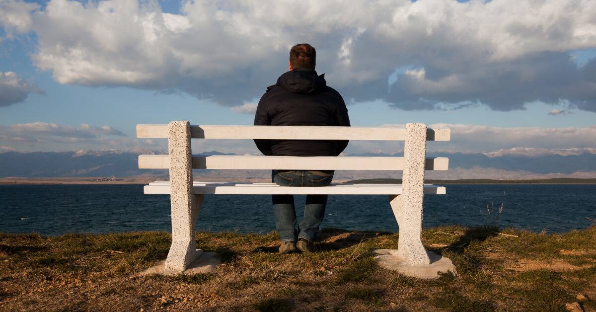 A man sitting alone on a bench looking out at the water.