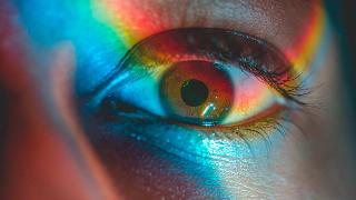 A close shot of an eye with rainbow light being shined across it.