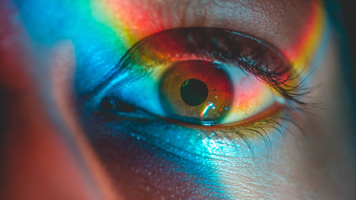 A close shot of an eye with rainbow light being shined across it.