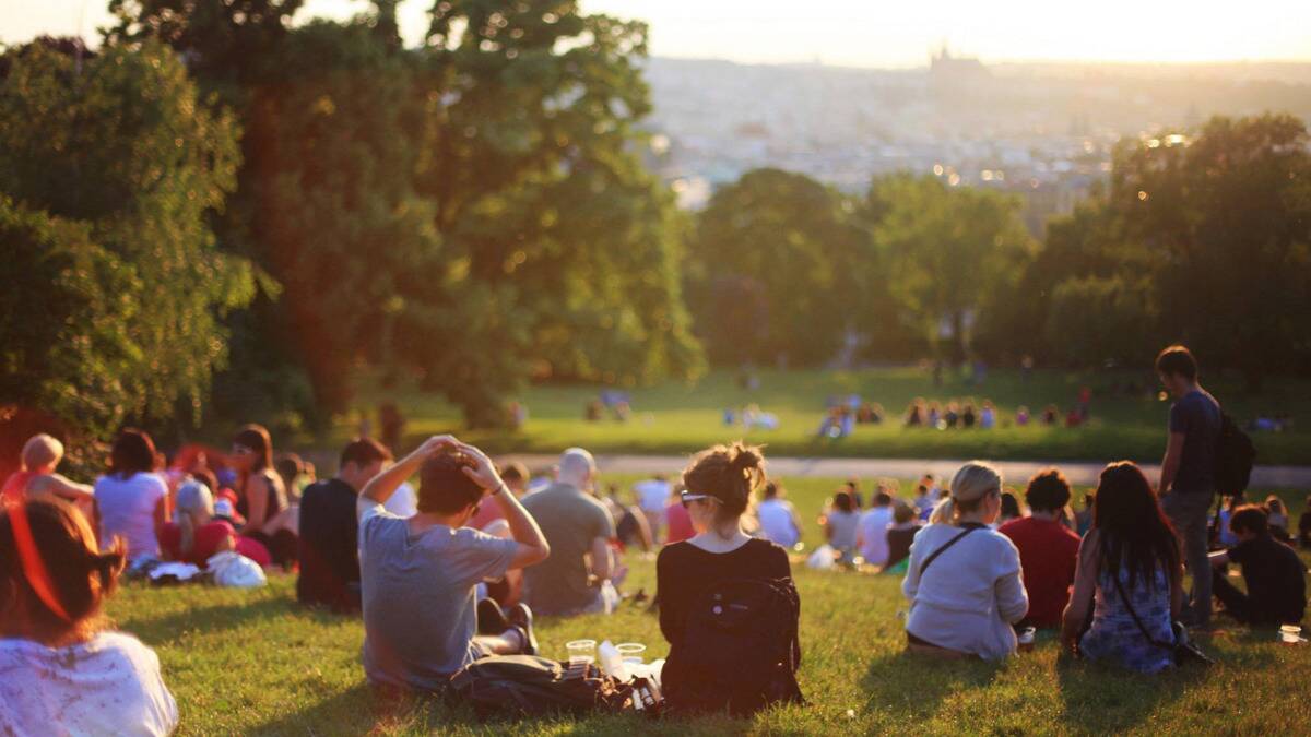 A gentle hill in a park, filled with people sitting in groups in the sunshine.