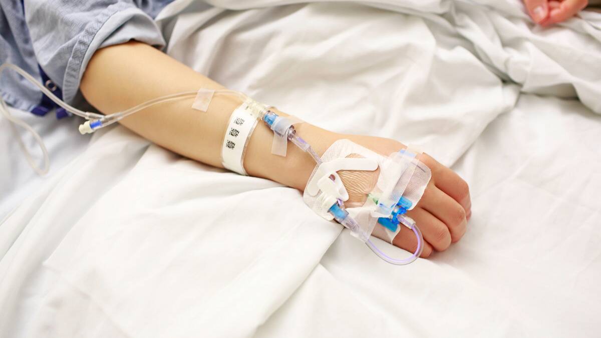 A hand with an IV drip in it, tubes taped up the patient's arm.