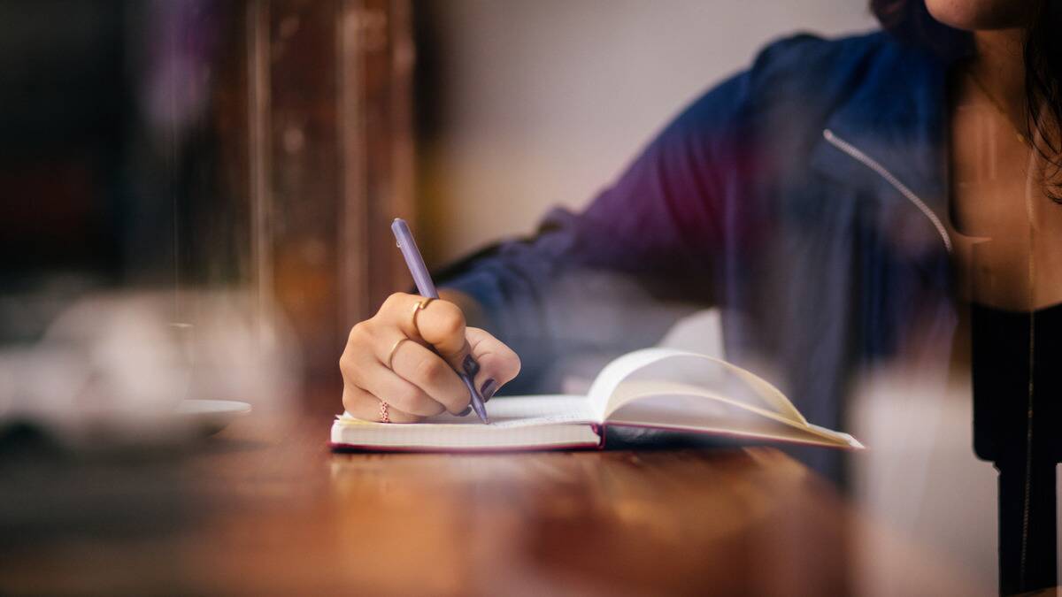 A woman writing in a journal, arm propped up on a table.