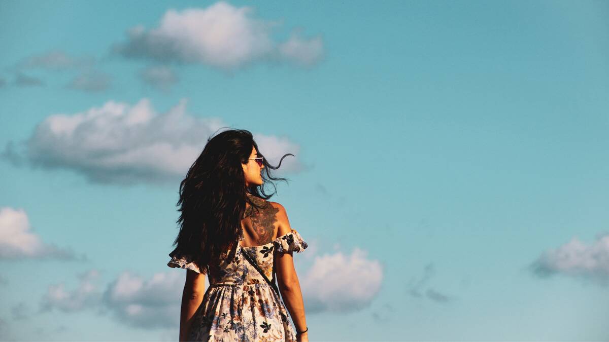 A woman standing in front of a vibrant blue sky, looking off to the side so we see her profile.