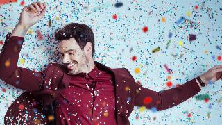 A man in a red suit dancing as confetti falls around him.