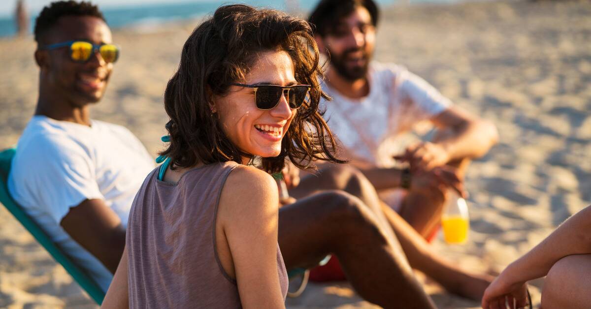 A woman smiling as she sits on the beach with her friends.