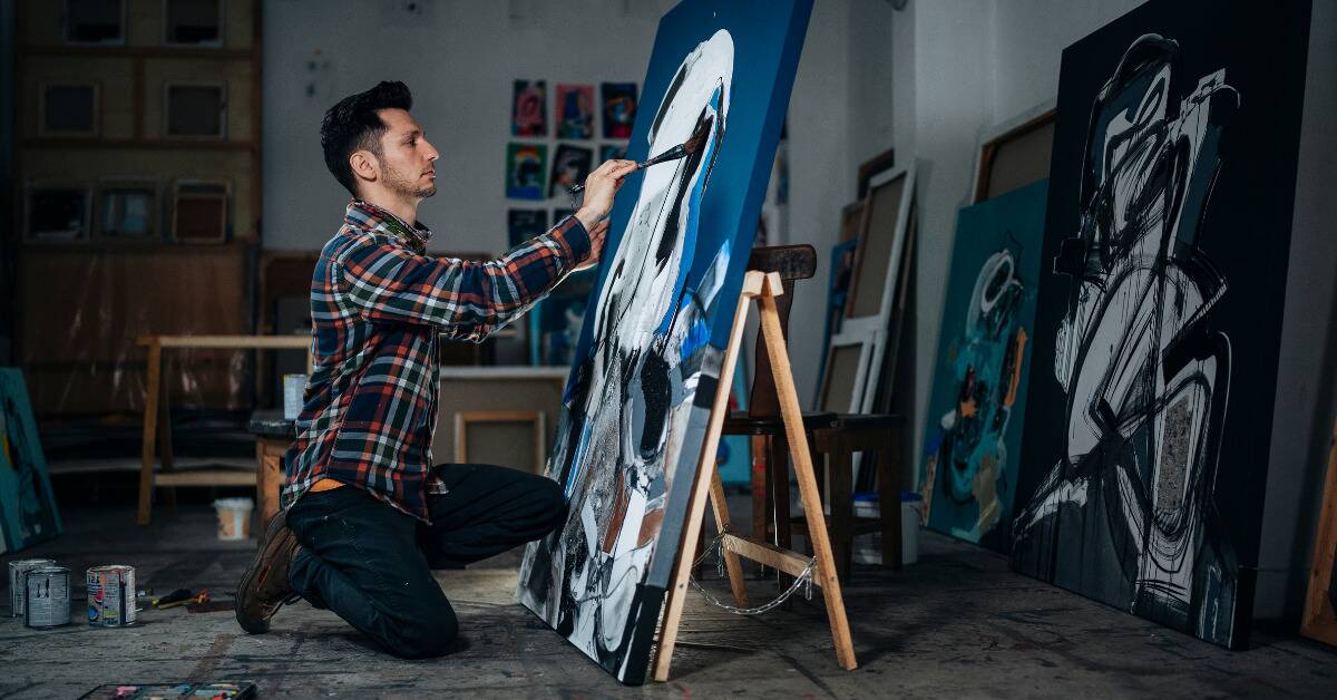 A man kneeling down to paint on a large canvas.