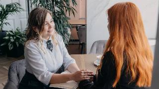 Two women talking, holing hands across the table and listening to one another.