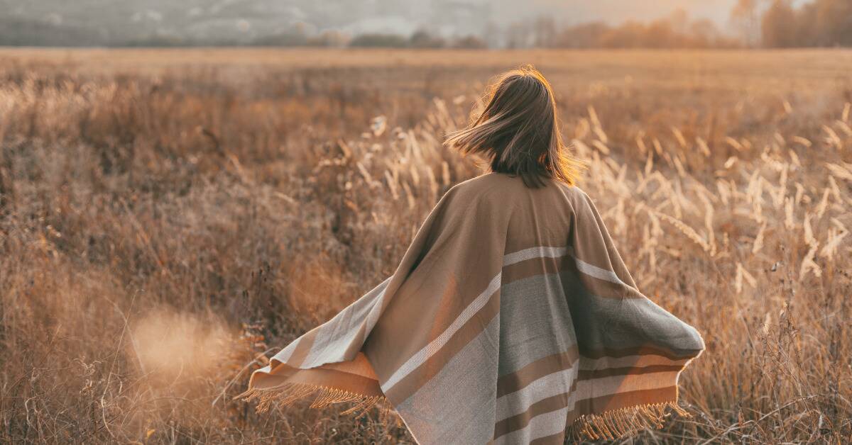 A woman in a poncho walking into a field of tall grass.