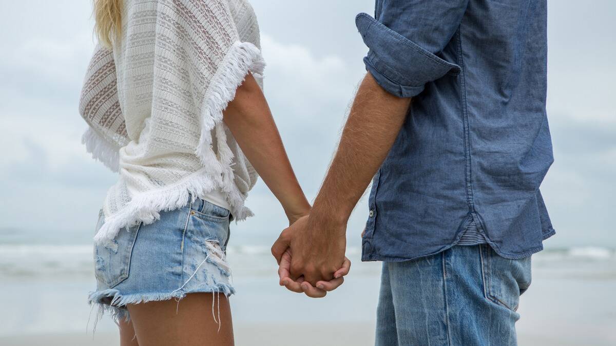 A close shot of a couple holding hands on the beach.
