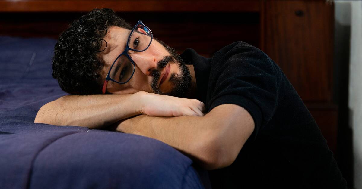 A man resting his head on his arms, which are also on his bed.