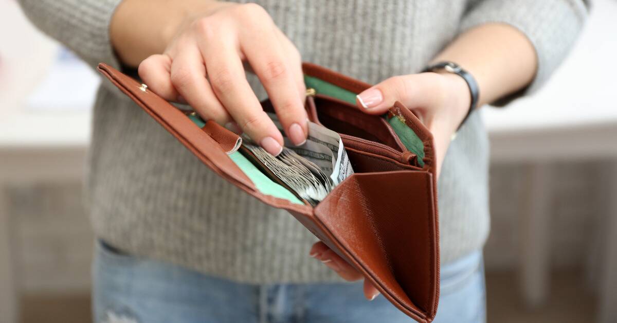 A woman flipping through bills in her open wallet.