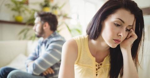 A woman with her head in her hand, looking rejected, while a man behind her is looking away with crossed arms.