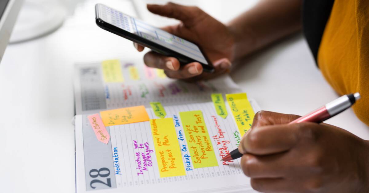 Someone copying down schedule information from a calendar on their phone to a physical journal.