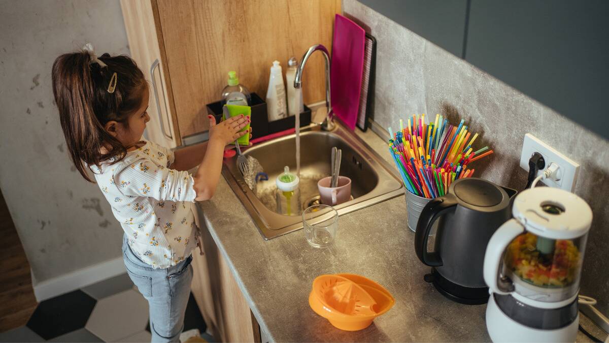 A young girl washing a fork in her kitchen sink.