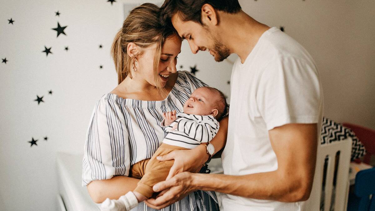 A couple holding their baby, foreheads together, smiling down at him.