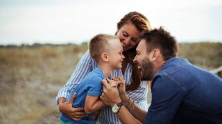 A mother and father having fun with their son outside, all smiling together.