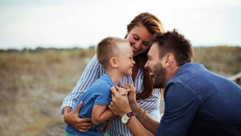 A mother and father having fun with their son outside, all smiling together.