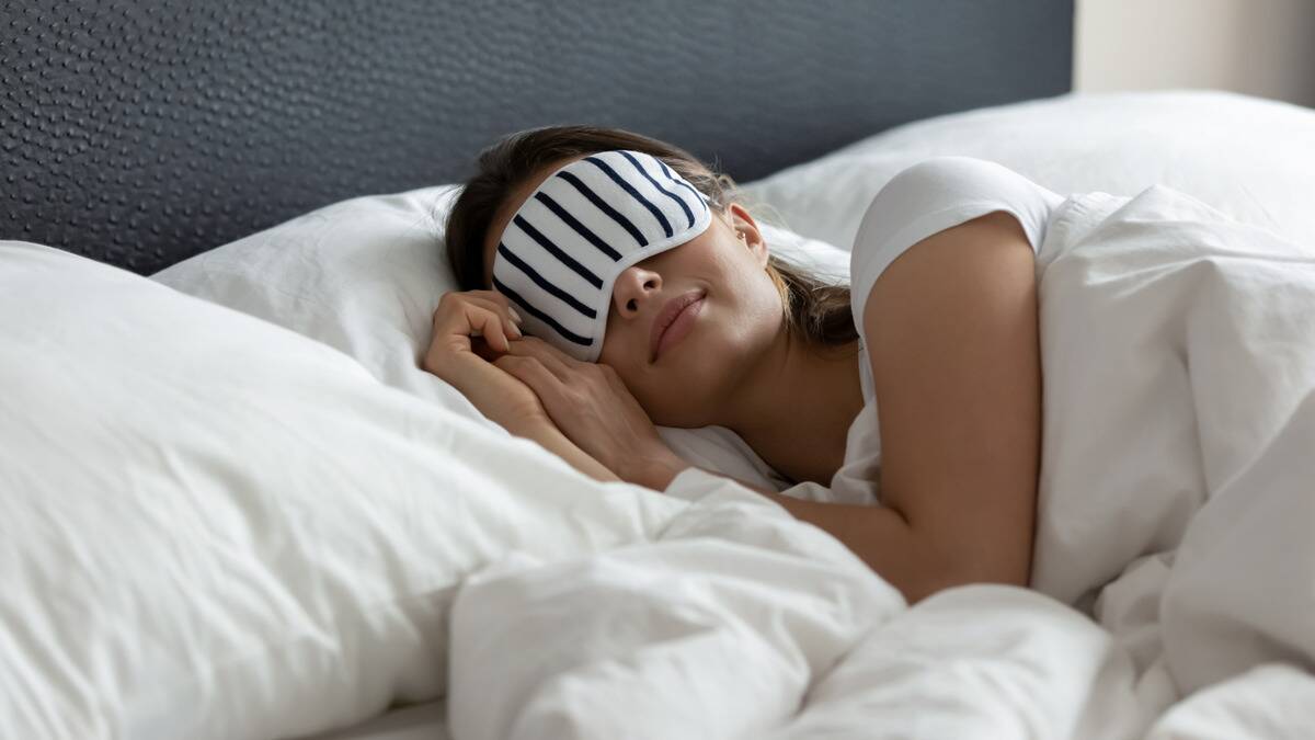 A woman laying in bed, smiling in her sleep, a white and black striped eyemask on.