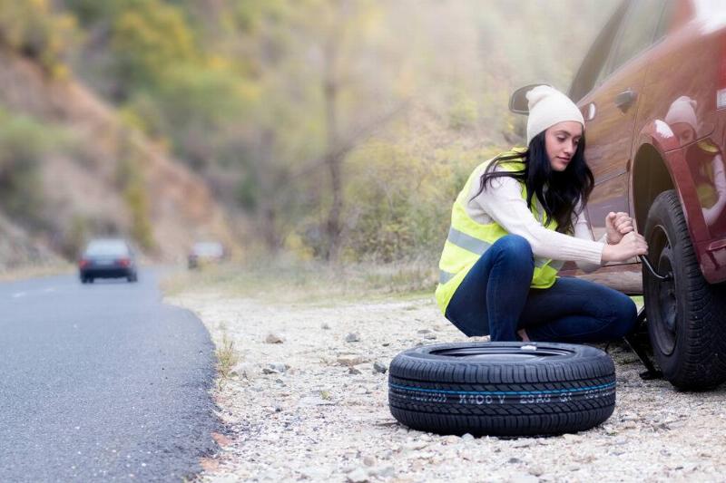 A woman changing a tire on the side of the road.