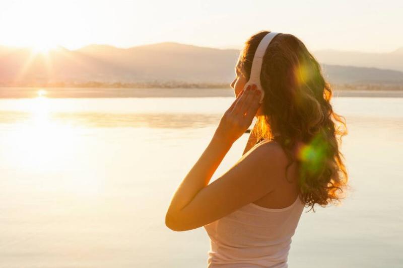 A woman listening to music while standing in the sunrise.