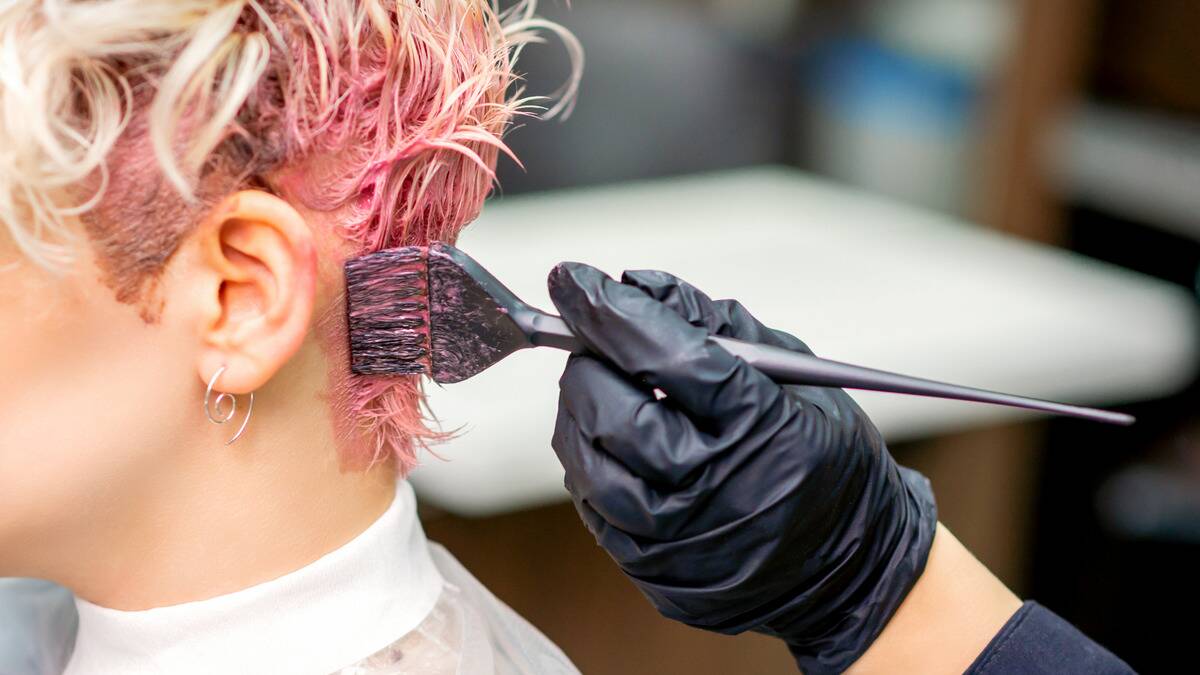 A hair stylist applying pink dye to their client's hair.