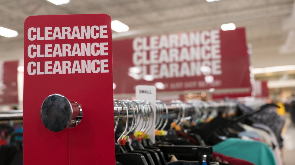 A clearance tag on a rack of clothing at a store, a larger clearance sign also seen in the background.