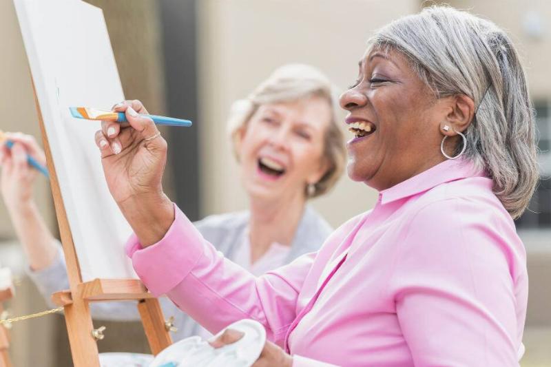 Two women smiling as they paint on canvases.