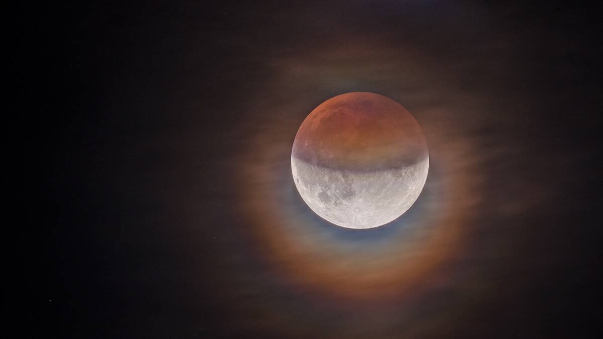 A partial lunar eclipse with a colorful light aura around it in the night sky.