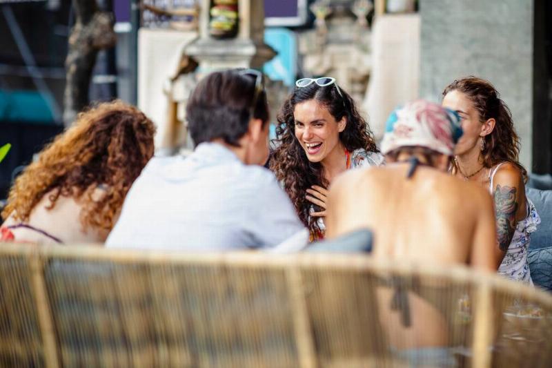 A group of friends sitting outside and laughing, one woman in particular in focus as she smiles.