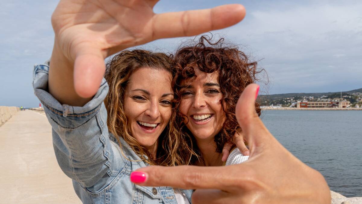 Two friends posing for a photo, standing very close together, each holding out a hand to make a rectangle shape with their fingers around their faces.