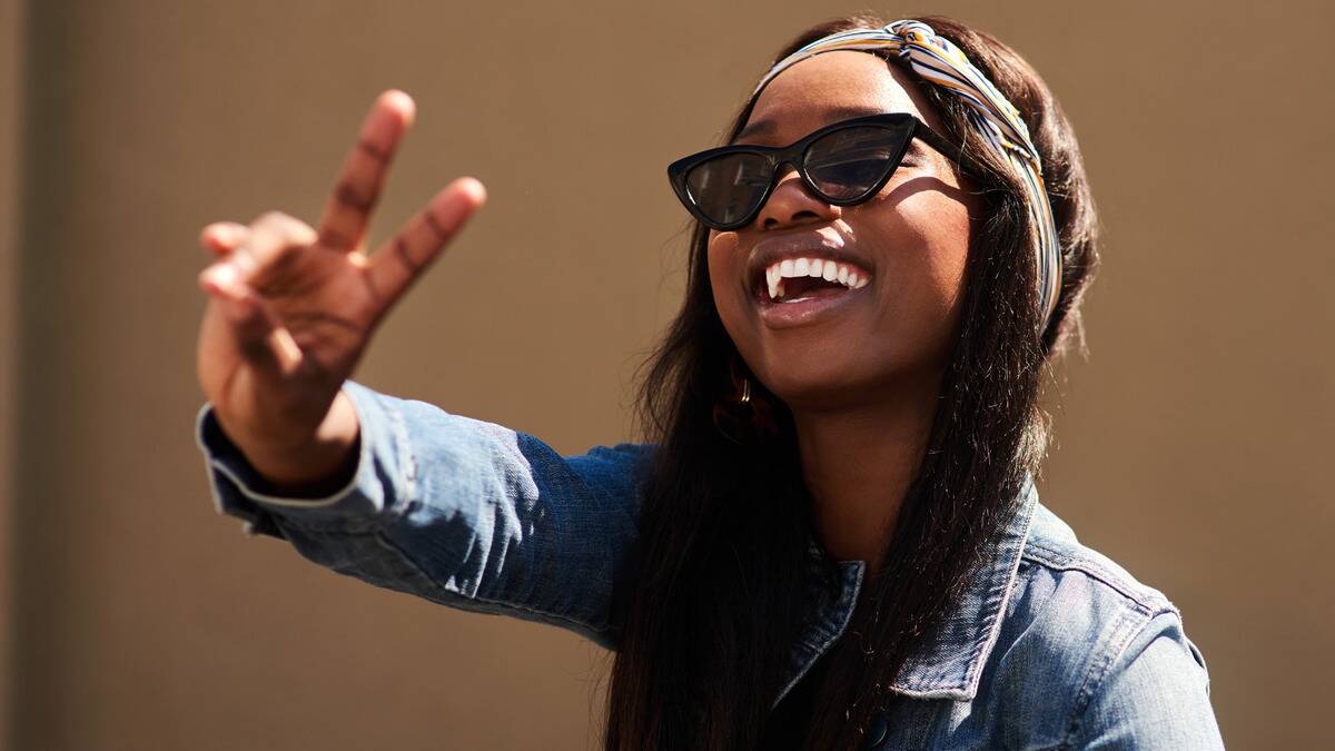 A woman standing in the light holding her hand out in a peace sign as she smiles.