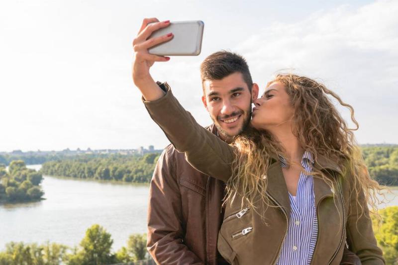 A couple taking a selfie, the woman kissing the man's cheek while the man smiles at the camera.