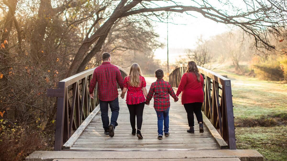 A family in matching red shirts all holding hands as they walk away from the camera across a wooden bridge.