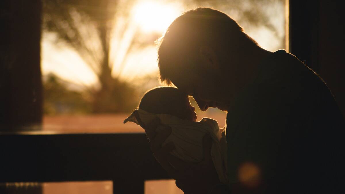 A silhouette of a father holding his baby close, their foreheads together, sun rising behind them.