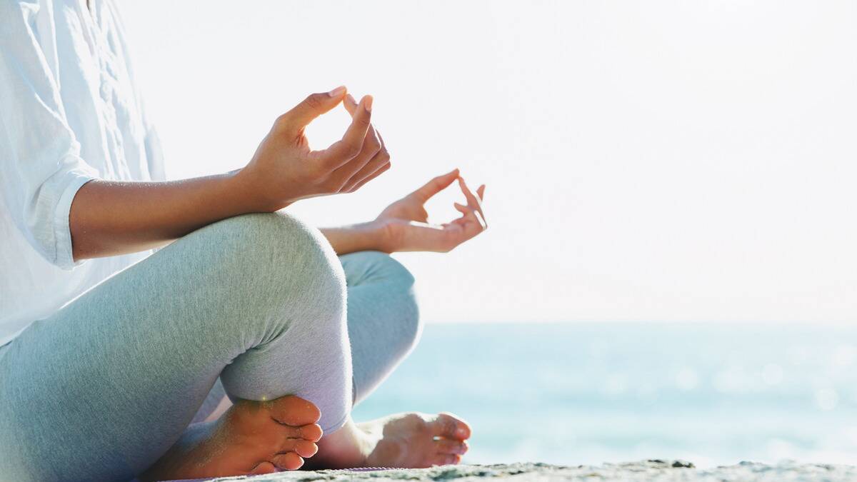 A close shot of someone meditating on a beach, hands poised on their knees.