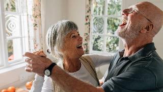 An older couple dancing in their home, both smiling and laughing.