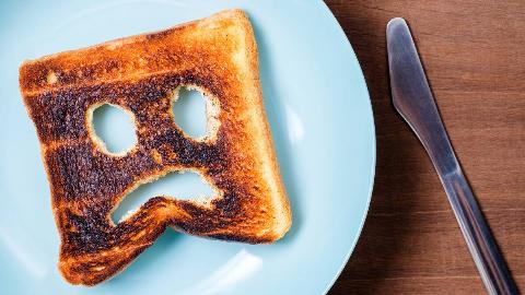 A piece of burnt toast on a light blue plate, pieces of the slice having either been bitten or cut out to resemble a frowning face.