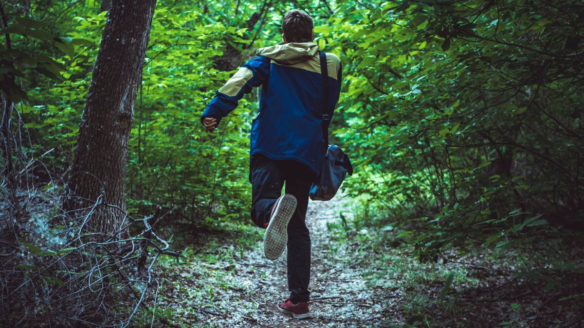 A man running away from the camera into a forest area.