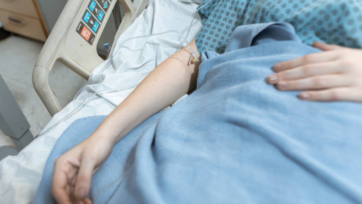 A close shot of someone laying in a hospital bed, an IV in their arm.