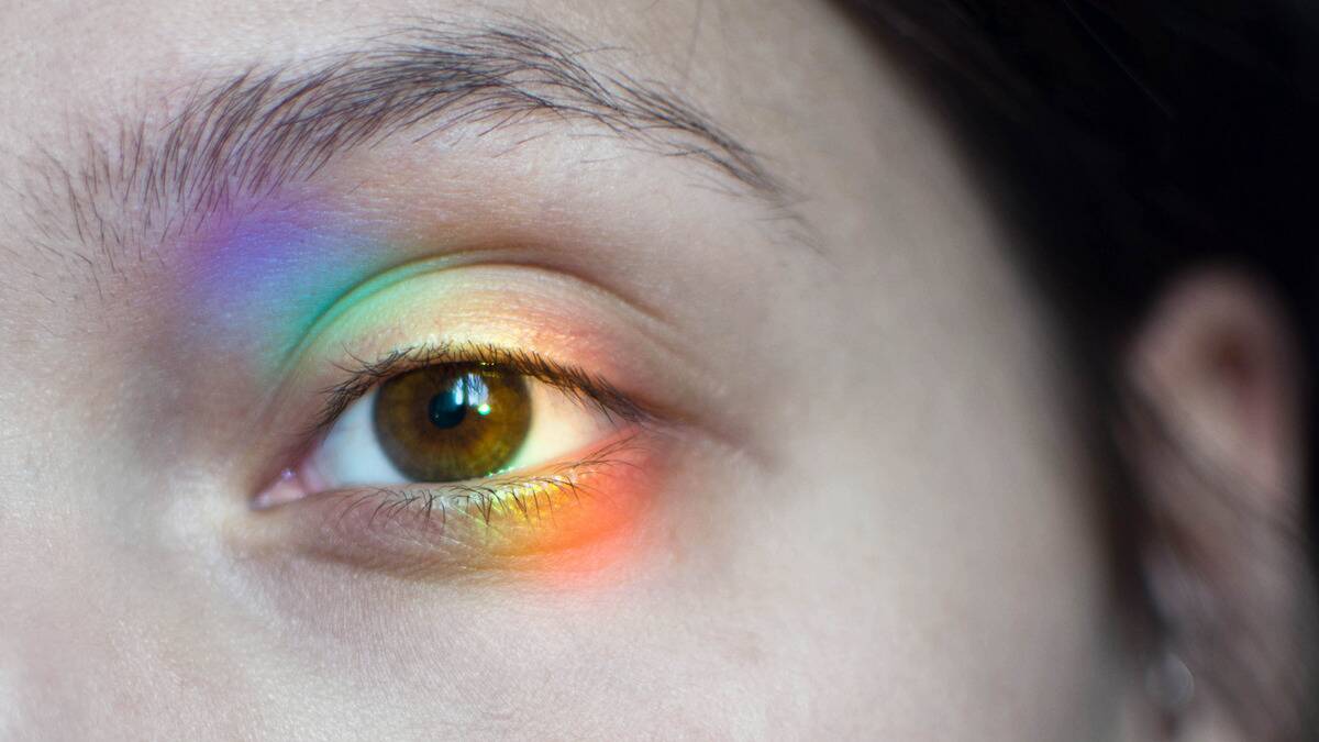 A close shot of a woman's eye with a rainbow-hued light shining on it.