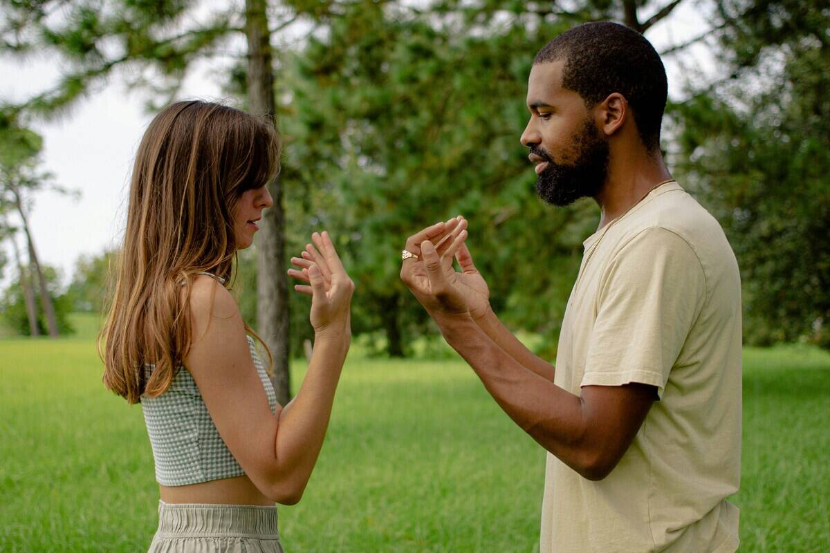 A couple outside, standing a few feet apart, both with their hands in front of them, seemingly participating in some sort of breathing exercise.