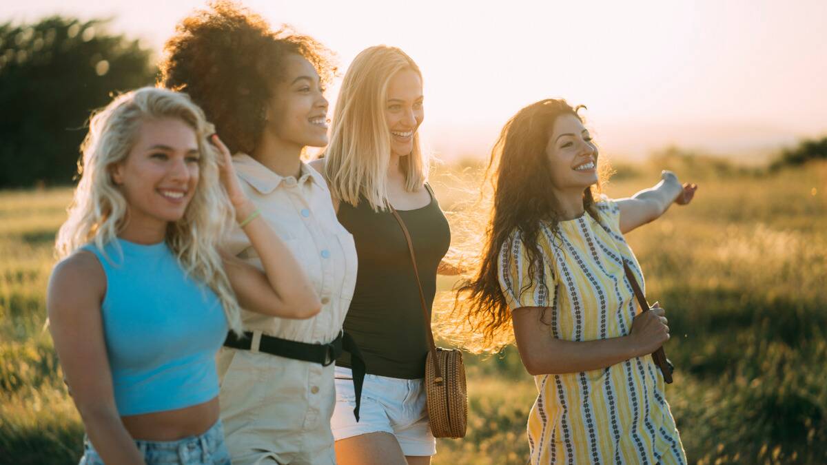 A group of four women walking through a field as the sun sets, smiling as they chat.